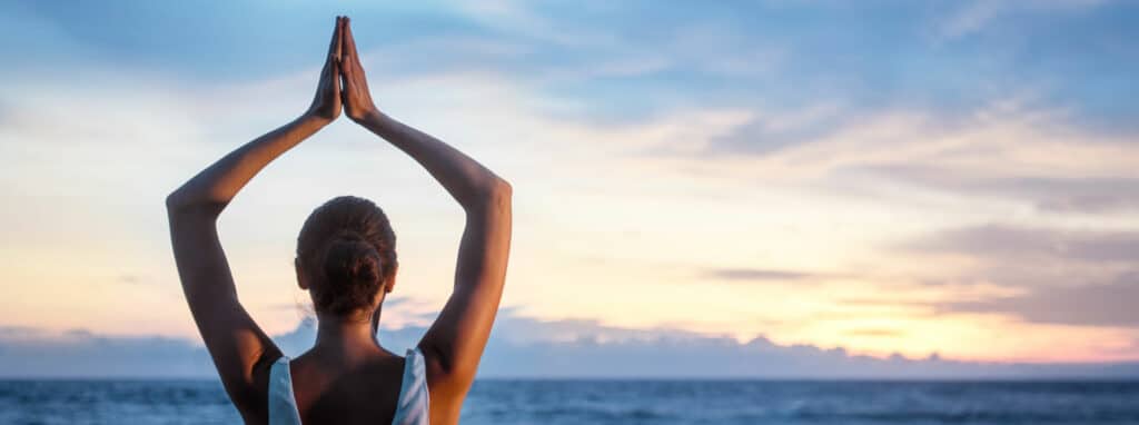 femme position de yoga sur une plage au coucher du soleil